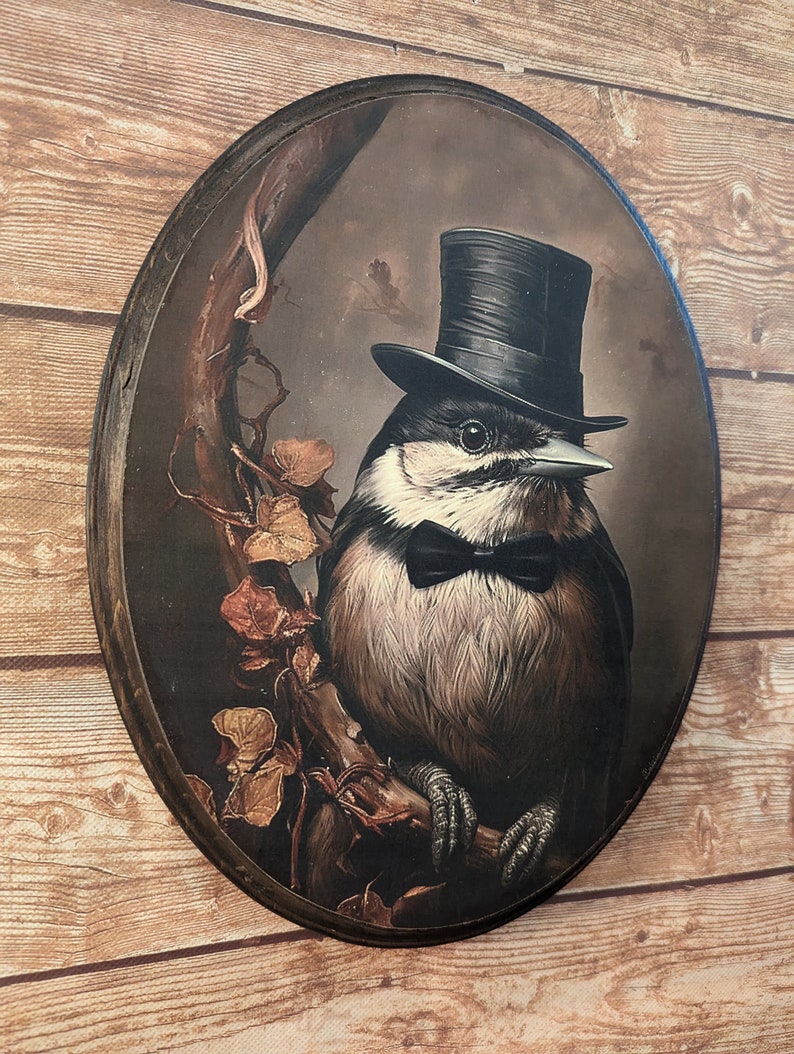 K&ouml;nnte beinhalten: Eine runde Holzplakette mit einem Gem&auml;lde eines Vogels, der einen schwarzen Zylinder und eine Fliege tr&auml;gt. Der Vogel sitzt auf einem Ast mit braunen und gelben Bl&auml;ttern. Der Hintergrund ist dunkelbraun.