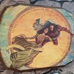 May include: A wooden plaque with a painted image of a man and woman flying through the air. The woman is wearing a long green dress and the man is wearing a red and blue robe. The plaque has a circular border with text in a foreign language.