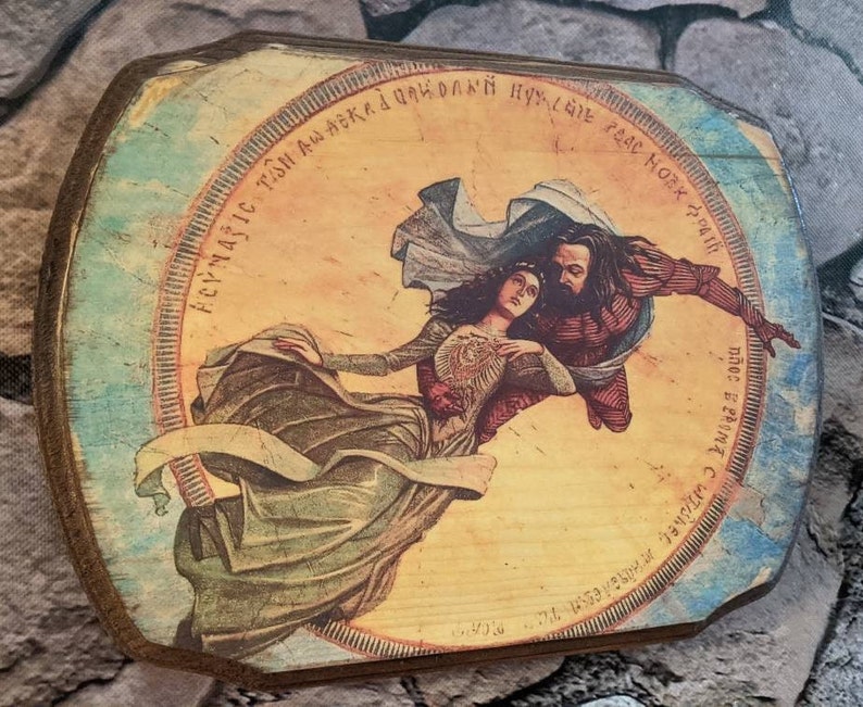 May include: A wooden plaque with a painted image of a man and woman flying through the air. The woman is wearing a long green dress and the man is wearing a red and blue robe. The plaque has a circular border with text in a foreign language.