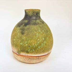 Op de afbeelding: Een handgemaakte keramische vaas met een afgeronde body en een smalle hals. De vaas heeft een gespikkelde groene glazuur over een tan basis, met een donkergroene en zwarte top. De vaas is ongeveer 15 cm hoog.