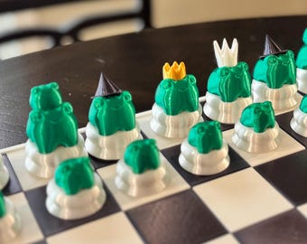 May include: A green and white chess set with frog-shaped pieces. The pieces are decorated with crowns, hats, and other whimsical details.