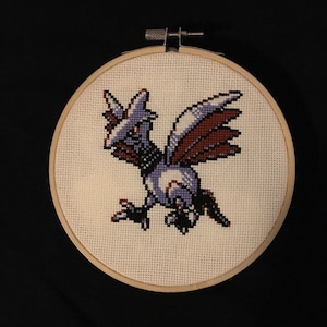 May include: A cross-stitch embroidery of a purple and blue bird with red wings, framed in a wooden hoop.