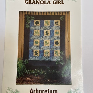 May include: A quilting pattern titled "Arboretum" by Granola Girl. The pattern features a quilt with a checkered design of blue and yellow squares with green leaf appliques. The quilt is framed by a wooden fence and surrounded by greenery.