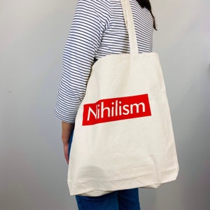 May include: A white tote bag with a red rectangle that says "Nihilism" in white letters.