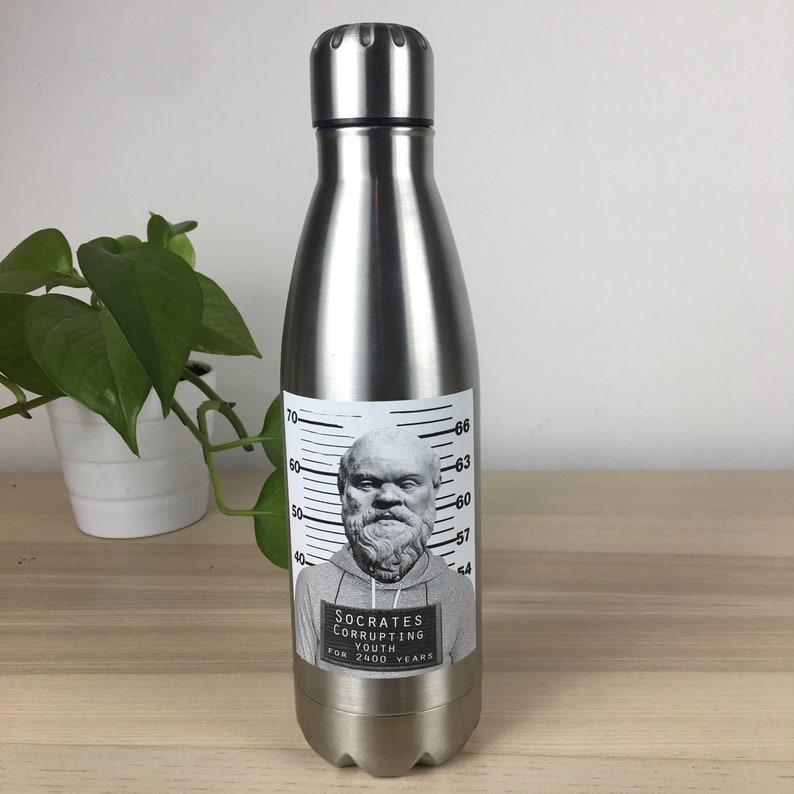 Puede incluir: Una botella de agua de acero inoxidable con una pegatina de foto policial en blanco y negro de S&oacute;crates. La pegatina dice "Socrates Corrupting Youth for 2400 Years".