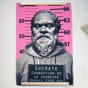 May include: A pink and black poster with a mugshot of a man with a beard and the text "SOCRATE CORRUPTION DE LA JEUNESSE DEPUIS 2400 ANS".