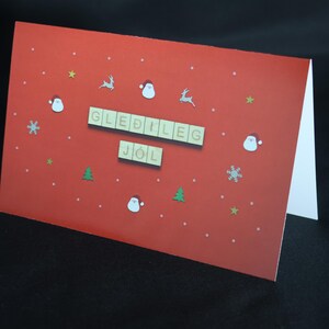 May include: A red Christmas card with the words "GLEDILIG JÓL" in wooden letter tiles. The card is decorated with white dots, snowflakes, stars, Santa faces, and reindeer.