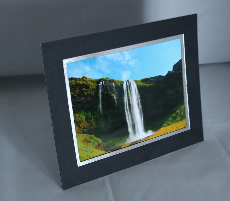 K&ouml;nnte beinhalten: Ein schwarzer Bilderrahmen mit silbernem Rand, der ein Foto eines Wasserfalls zeigt, der eine gr&uuml;ne Klippe hinunterst&uuml;rzt.