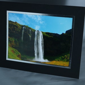 K&ouml;nnte beinhalten: Ein Foto eines Wasserfalls, der eine felsige Klippe hinunterst&uuml;rzt. Der Wasserfall ist umgeben von &uuml;ppiger gr&uuml;ner Vegetation und einem blauen Himmel mit wei&szlig;en Wolken.