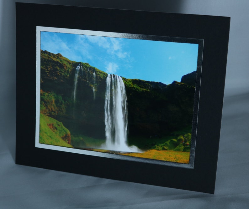 K&ouml;nnte beinhalten: Ein Foto eines Wasserfalls, der eine felsige Klippe hinunterst&uuml;rzt. Der Wasserfall ist umgeben von &uuml;ppiger gr&uuml;ner Vegetation und einem blauen Himmel mit wei&szlig;en Wolken.