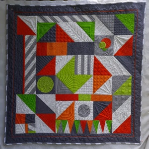 May include: A colorful quilt with a geometric pattern. The quilt is made up of squares and triangles in shades of gray, green, orange, and red. The quilt is quilted with a variety of designs, including swirls, circles, and lines.