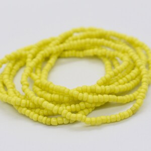 May include: A yellow beaded waist bead necklace. The beads are small and tightly woven together, creating a smooth and continuous look.