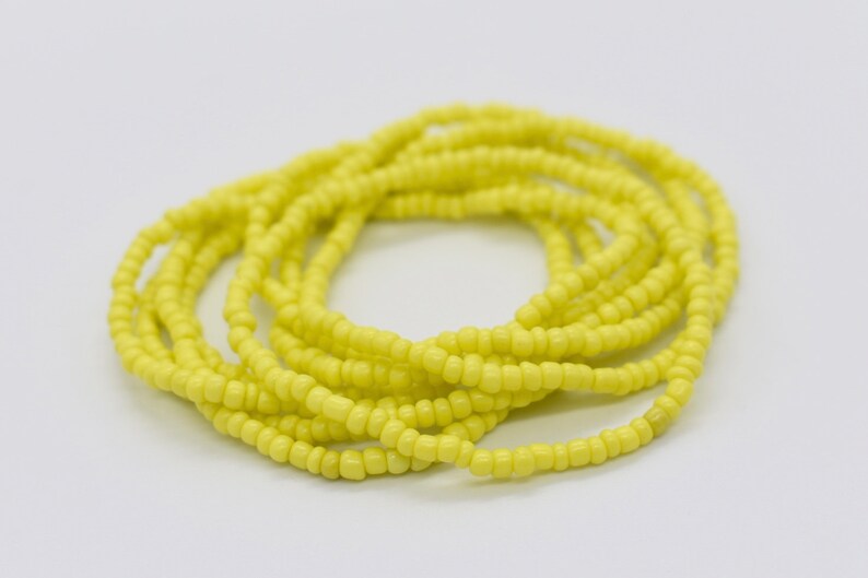 May include: A yellow beaded waist bead necklace. The beads are small and tightly woven together, creating a smooth and continuous look.