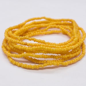May include: A yellow beaded waist chain, also known as a waist bead or belly chain, is coiled on a white surface.