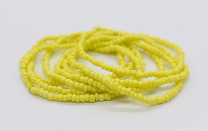 May include: A yellow beaded waist bead necklace, also known as a waist chain, is made of small, round beads strung together. The beads are a bright, vibrant yellow color and are arranged in a simple, elegant design.