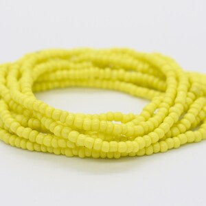 May include: A yellow beaded bracelet, made of small, round beads, is coiled up in a circle.