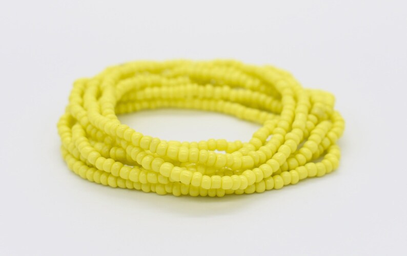 May include: A yellow beaded bracelet, made of small, round beads, is coiled up in a circle.