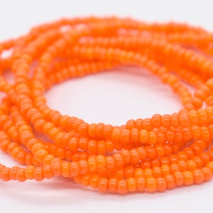 May include: A close-up of a long strand of orange seed beads. The beads are small and round, and they are strung together in a continuous loop.