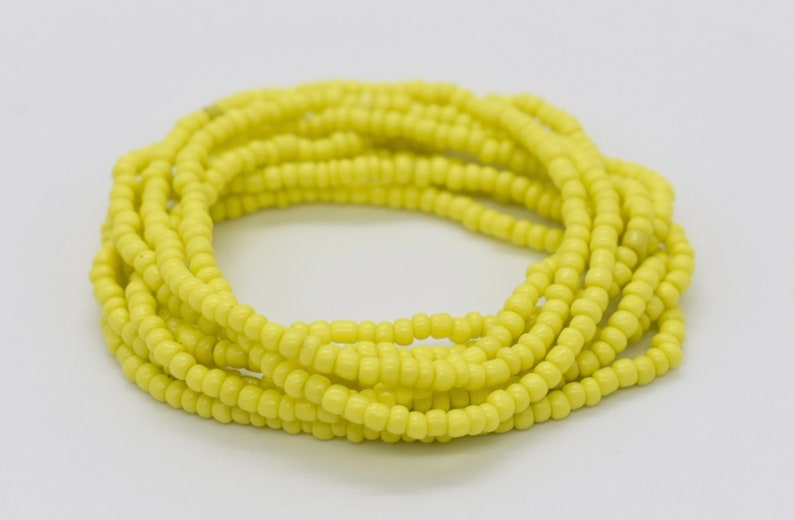 May include: A yellow beaded waist bead, also known as a waist chain, is a string of beads worn around the waist. The beads are small and uniform in size, creating a smooth and continuous look.