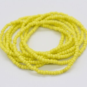 May include: A yellow beaded bracelet made of small, round beads. The bracelet is coiled up and ready to be worn.