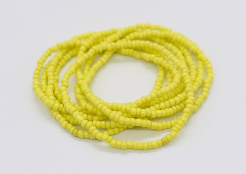 May include: A yellow beaded bracelet made of small, round beads. The bracelet is coiled up and ready to be worn.