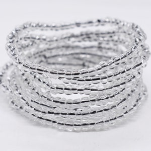 May include: A coiled bracelet made of numerous strands of small, clear beads with a silver-like sheen. The beads are tightly strung together, creating a textured, layered effect. The bracelet is set against a plain white background.
