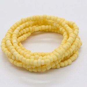 May include: A close-up of a coiled strand of pale yellow beads. The beads are small and round, and they are strung together on a clear thread.