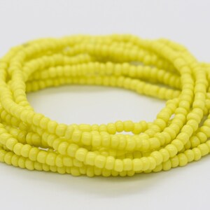 May include: A yellow beaded bracelet made of small, round beads. The bracelet is coiled up and ready to be worn.