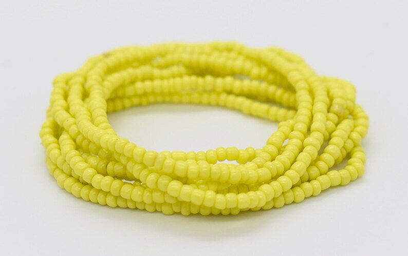 May include: A yellow beaded bracelet made of small, round beads. The bracelet is coiled up and ready to be worn.