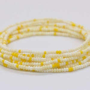 May include: A white and yellow beaded waist beads, also known as waist beads or belly beads, are coiled up on a white surface.