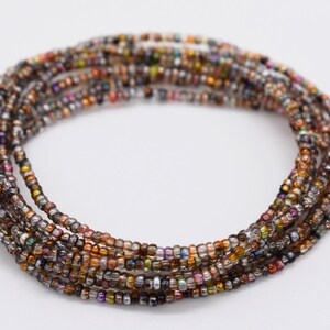 Pode incluir: Um bracelete de contas multicolorido com uma variedade de contas de vidro iridescente em tons de marrom, prata e dourado.
