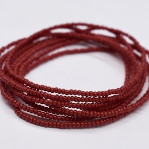 May include: A close-up of a terracotta-colored beaded waist chain. The chain is made of small, round beads that are strung together in a continuous loop.
