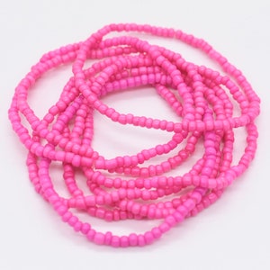 Puede incluir: Un conjunto de pulseras de cuentas rosadas, apiladas y enrolladas juntas. Las pulseras est&aacute;n hechas de peque&ntilde;as cuentas redondas que est&aacute;n enhebradas en un cord&oacute;n delgado.