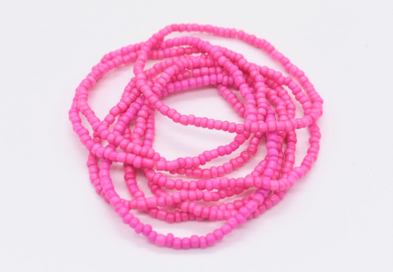 Puede incluir: Un conjunto de pulseras de cuentas rosadas, apiladas y enrolladas juntas. Las pulseras est&aacute;n hechas de peque&ntilde;as cuentas redondas que est&aacute;n enhebradas en un cord&oacute;n delgado.