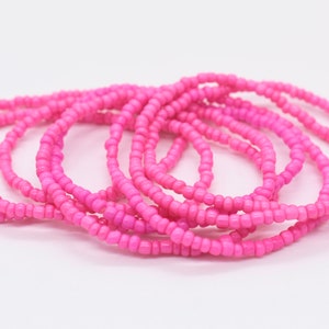Puede incluir: Un conjunto de pulseras de cuentas rosadas, apiladas y dispuestas en un patr&oacute;n circular. Las pulseras est&aacute;n hechas de peque&ntilde;as cuentas redondas que se ensartan para crear un bucle continuo.