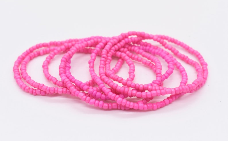 Puede incluir: Un conjunto de pulseras de cuentas rosadas, apiladas y dispuestas en un patr&oacute;n circular. Las pulseras est&aacute;n hechas de peque&ntilde;as cuentas redondas que se ensartan para crear un bucle continuo.