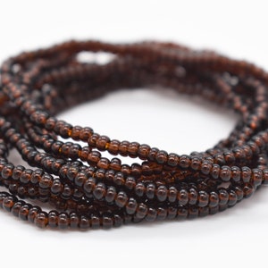 May include: A close-up of a brown beaded bracelet. The bracelet is made of small, round beads that are strung together on a thin cord. The bracelet is coiled up and is ready to be worn.
