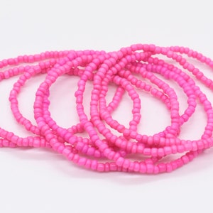 Puede incluir: Un conjunto de pulseras de cuentas rosadas, apiladas y dispuestas en un patr&oacute;n circular. Las pulseras est&aacute;n hechas de cuentas peque&ntilde;as y uniformes, creando una textura suave y consistente.
