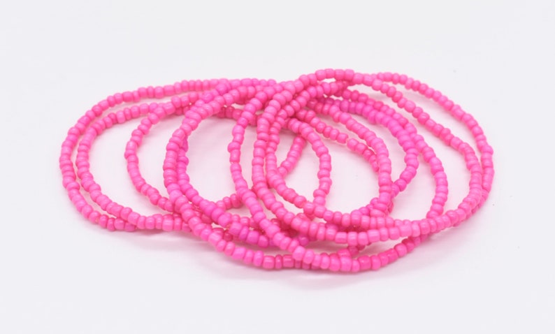 Puede incluir: Un conjunto de pulseras de cuentas rosadas, apiladas y dispuestas en un patr&oacute;n circular. Las pulseras est&aacute;n hechas de cuentas peque&ntilde;as y uniformes, creando una textura suave y consistente.