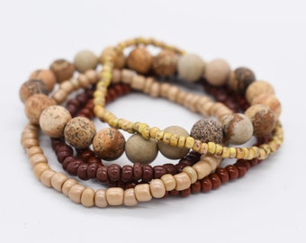 May include: A set of four bracelets made with brown, beige, and yellow beads. The bracelets are layered on top of each other.