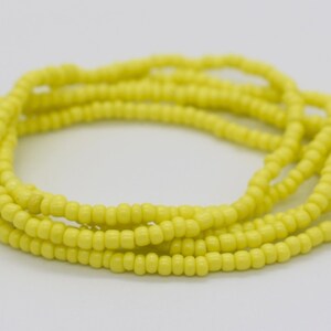 May include: A yellow beaded waist bead necklace. The beads are small and uniform in size, creating a smooth and continuous look.
