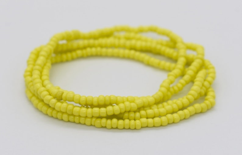May include: A yellow beaded waist bead necklace. The beads are small and uniform in size, creating a smooth and continuous look.