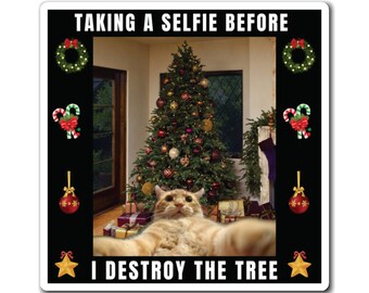 May include: A square sticker with a black border features a cat taking a selfie in front of a Christmas tree. Text reads "TAKING A SELFIE BEFORE I DESTROY THE TREE." Festive decorations surround the image.