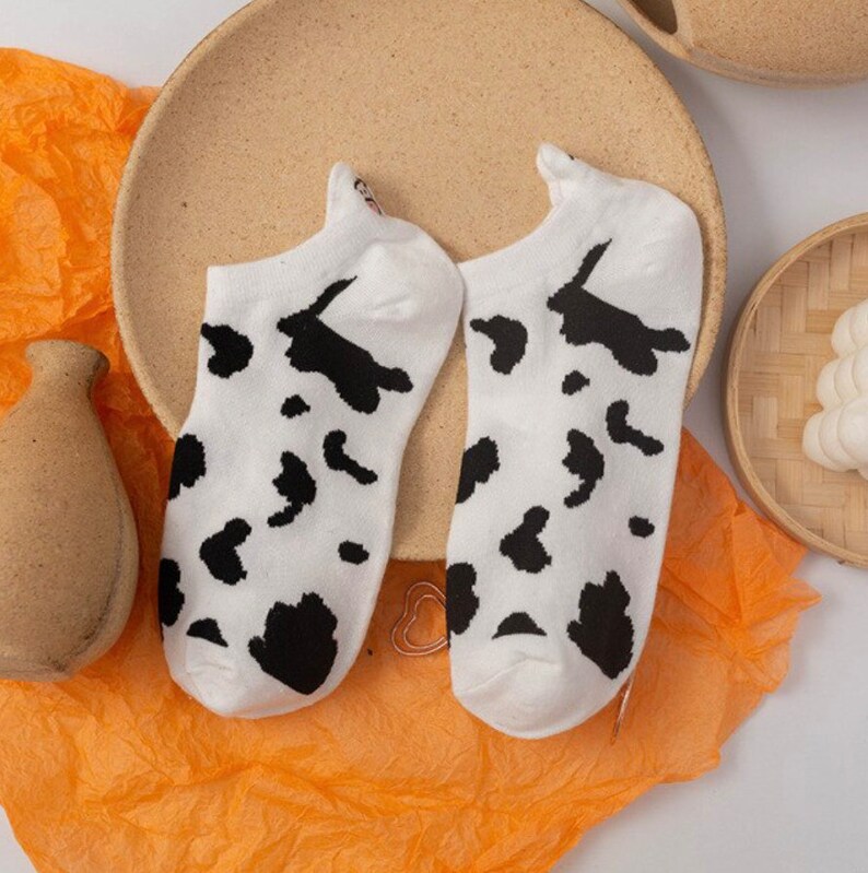 Pu&ograve; includere: Un paio di calzini alla caviglia bianchi con un motivo a mucca nero. I calzini sono realizzati in un materiale morbido e sono progettati per essere indossati con le scarpe. Un accessorio divertente e giocoso.