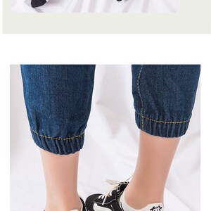Pu&ograve; includere: Scarpe da ginnastica bianche e nere con calzini bianchi con una grafica di una mucca. I calzini sono abbinati a pantaloni cropped in denim blu scuro con polsini elasticizzati. La parte superiore dell'immagine mostra calzini a righe bianche e nere.