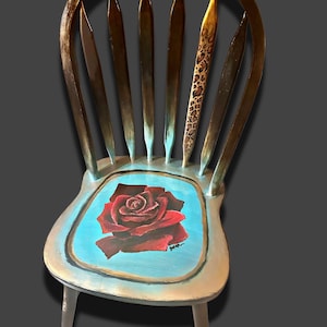 May include: A painted wooden chair with a floral design. The seat has a red rose on a light blue background. One of the chair's back slats has a leopard print. The chair is painted in brown, gold, and blue hues.