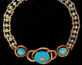 May include: A gold necklace with turquoise stones. The necklace has a large oval-shaped pendant with turquoise stones and a smaller oval-shaped pendant with turquoise stones.