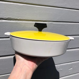May include: White and yellow enamel casserole dish with a black knob on the lid.