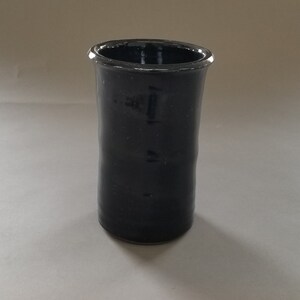 May include: A dark blue ceramic vase with a cylindrical shape. The vase has a smooth, glossy finish.
