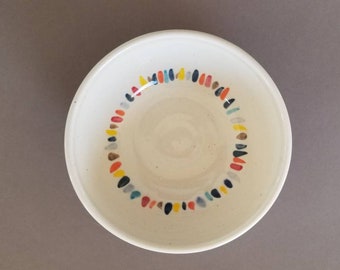May include: A white ceramic bowl with a colorful, speckled design around the rim. The bowl is empty and has a slight sheen.